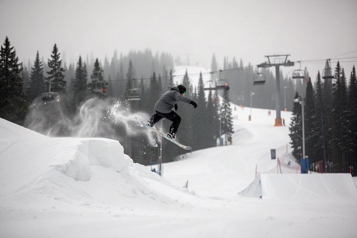 Snowboarder che salta da un side hit accanto a una pista battuta della stazione sciistica