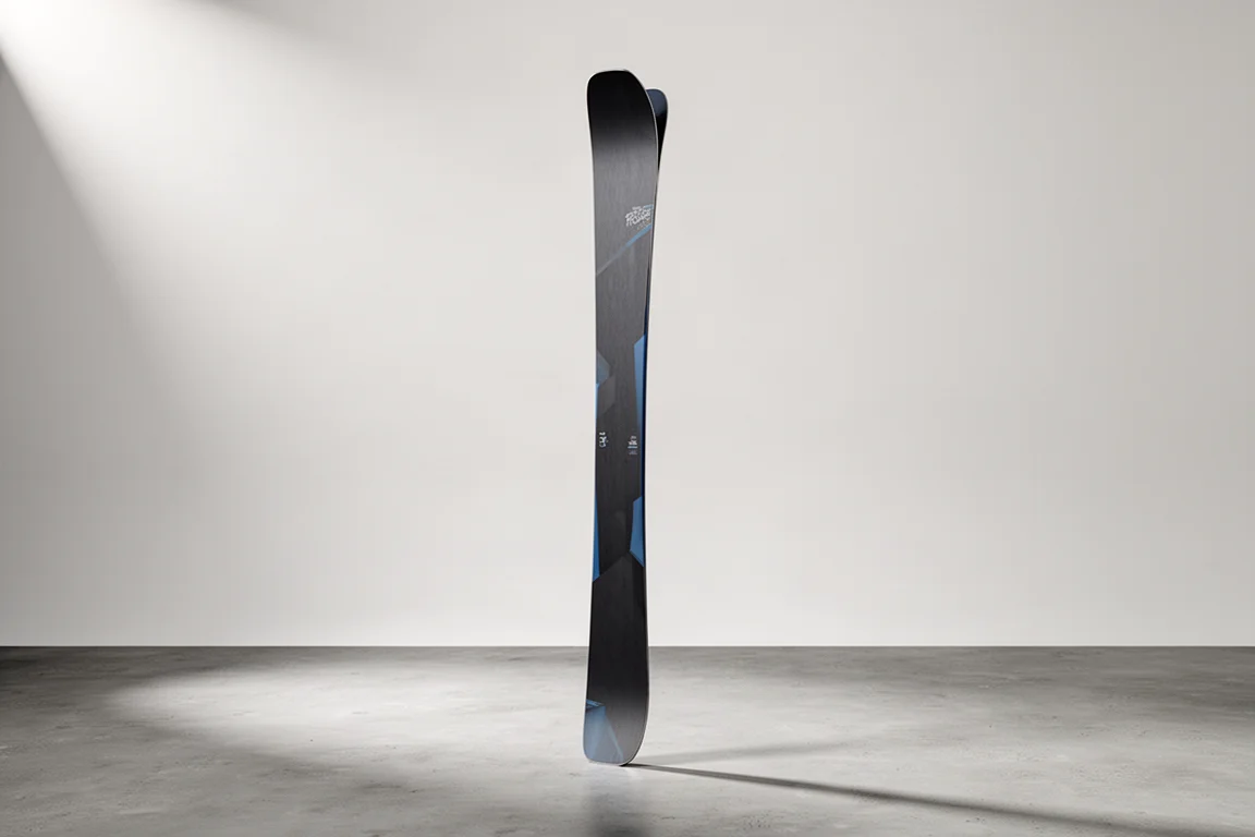 Wide freeride touring ski standing upright on concrete against a grey backdrop