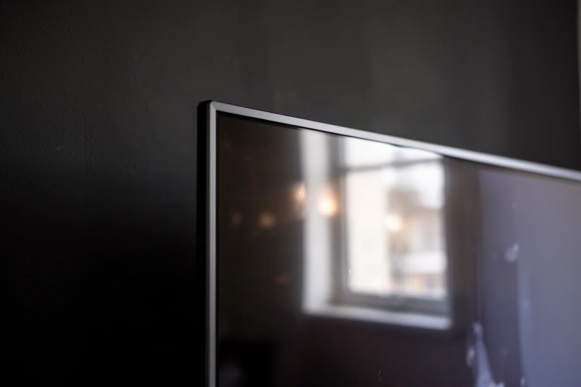 Primer plano de la esquina de un panel de televisor delgado con reflejos abstractos brillantes sobre una pared oscura
