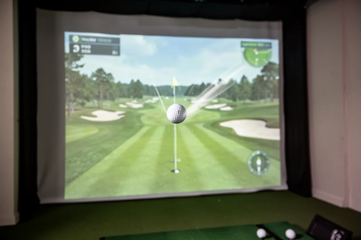 Golfboll som flyger mot ett grönt mål på en simulatorskärm med en smal fairway