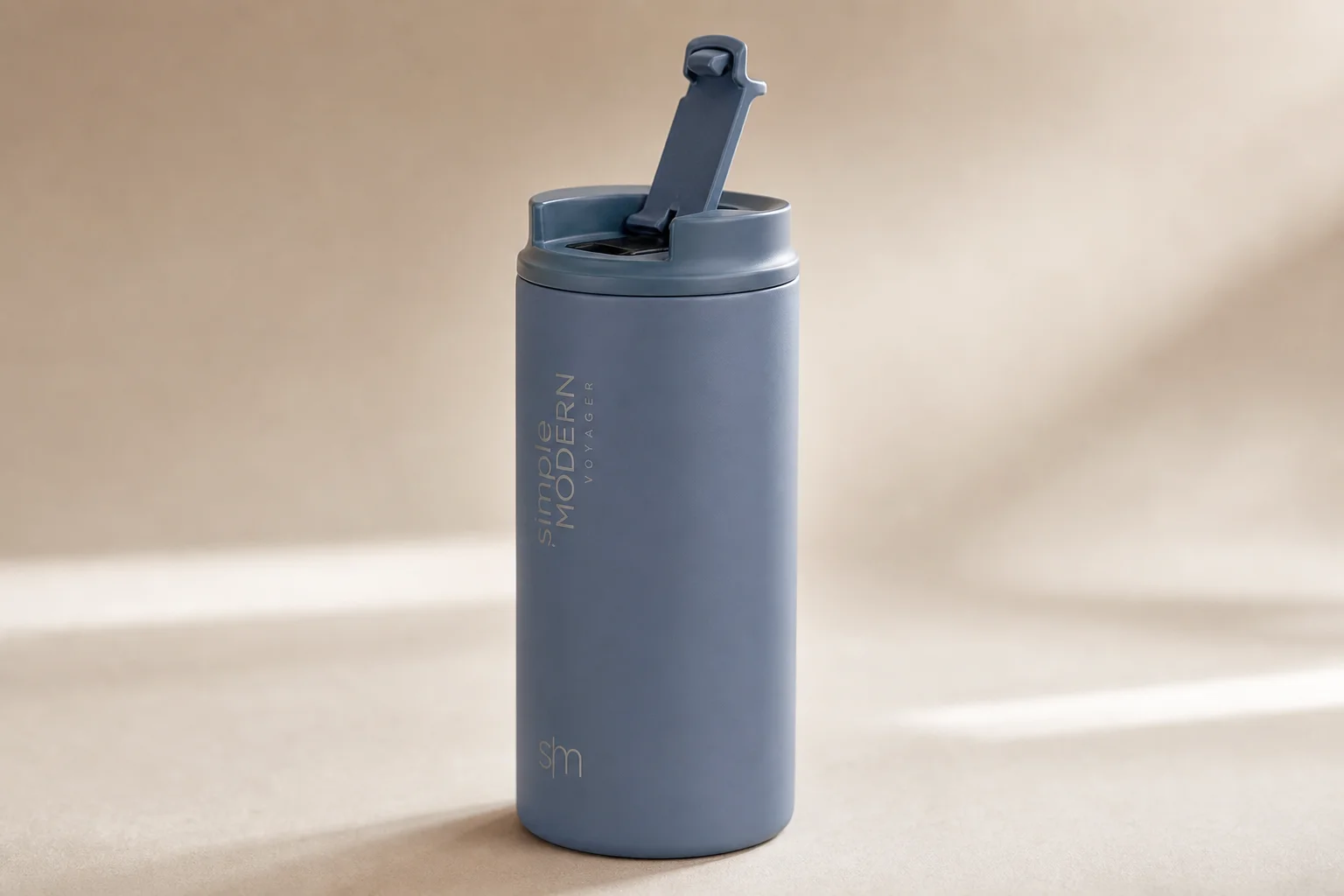 Nine insulated travel mugs arranged on concrete surface in various styles and colors