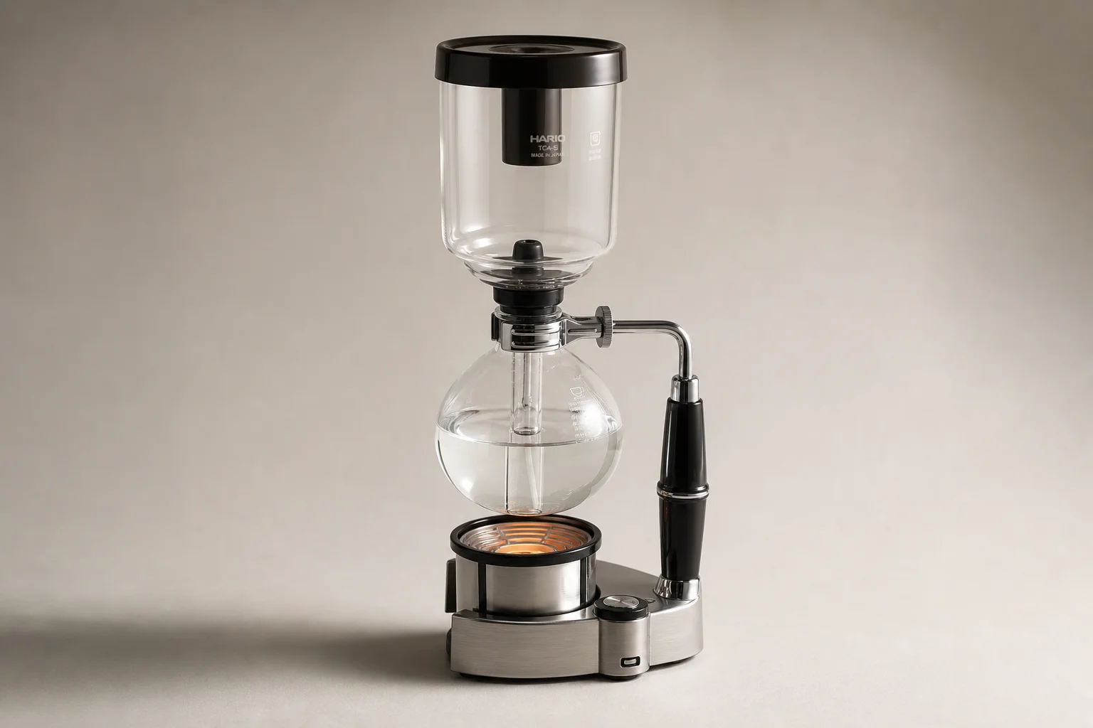 Modern HARIO siphon coffee brewer with glass chambers and heat lamp on neutral background