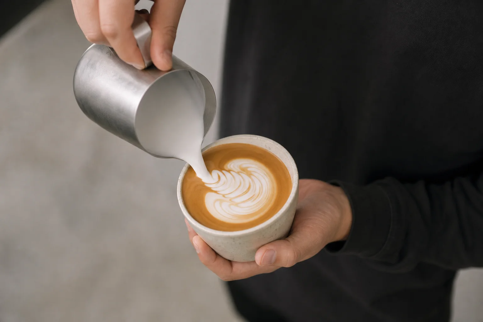 Barista pouring steamed milk into espresso to create latte art