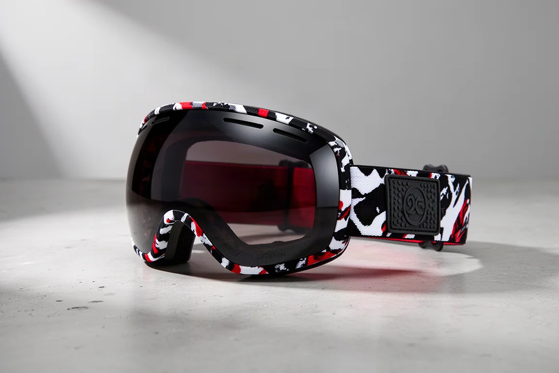 Snowboardbrille mit schwarzem, weißem und rotem Riemen auf einer Betonoberfläche