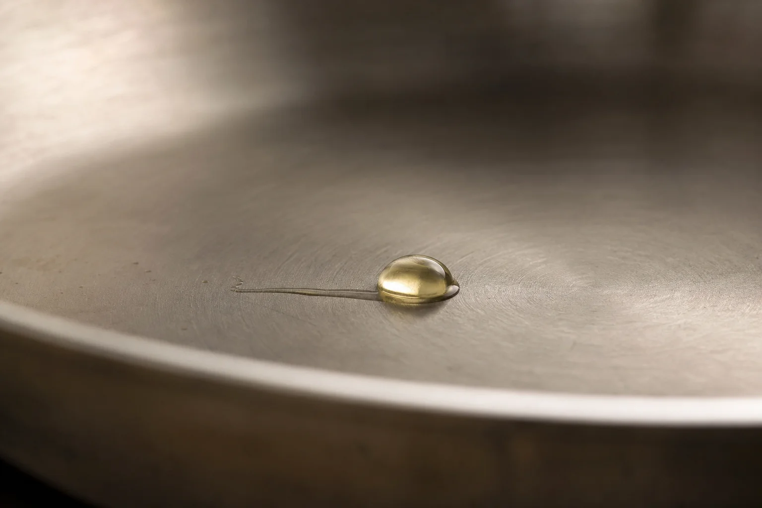 Gota de aceite formando una perla en la superficie de una sartén de acero inoxidable precalentada