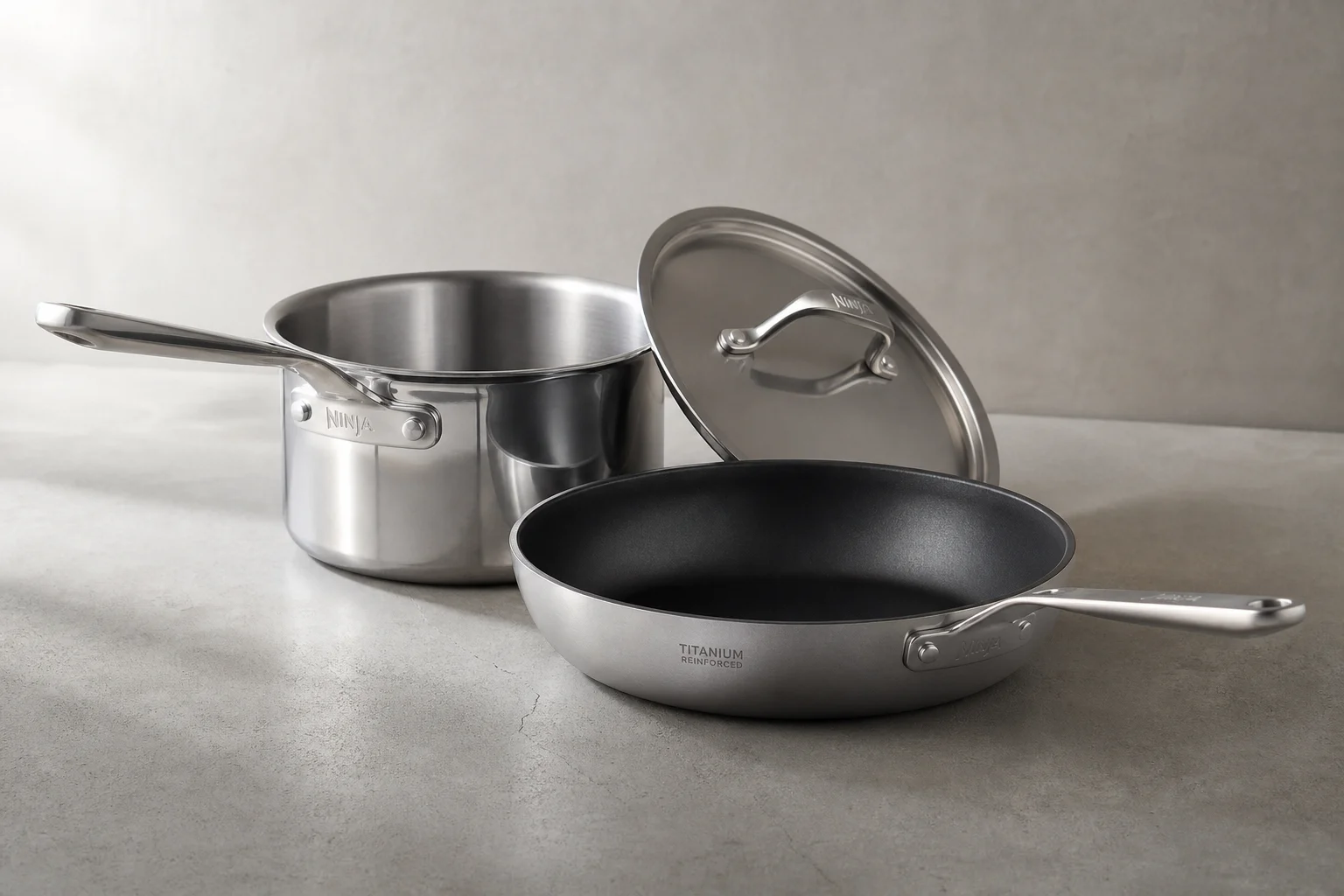 Hestan stainless steel and titanium cookware with universal lid on concrete surface