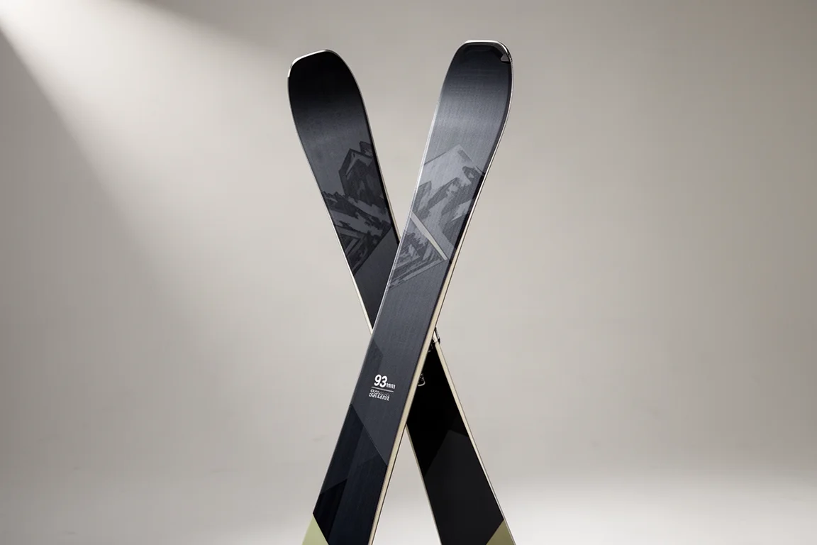 Pair of dark all-mountain skis standing upright on a neutral grey studio backdrop