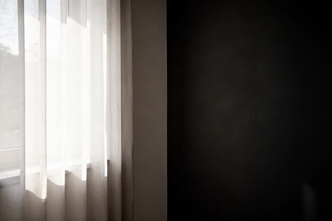 Extreme contrast between a bright sunlit window and deep shadow in a quiet interior