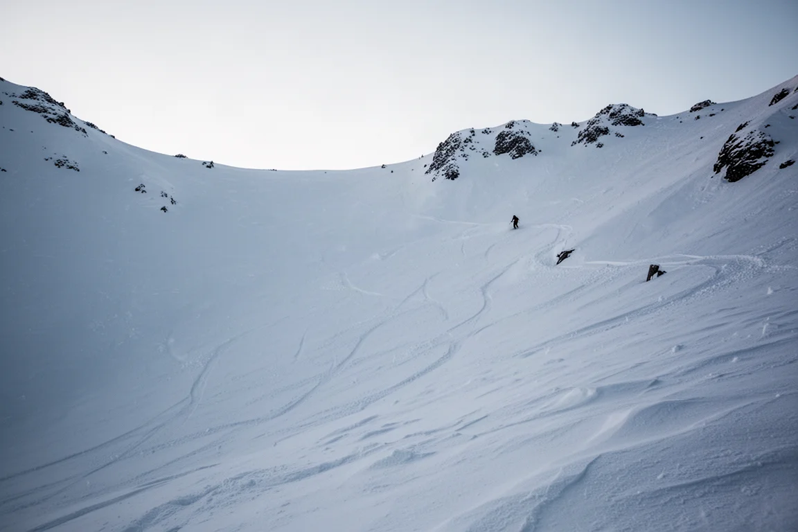 Steiler offener Alpin-Powderhang bei Morgengrauen mit entfernter Fahrersilhouette
