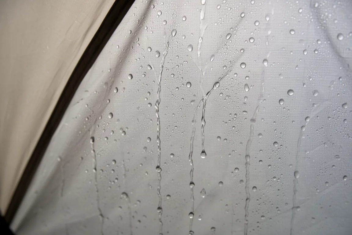 Gouttelettes de condensation recouvrant l'intérieur d'un tissu d'abri léger et humide dans une lumière froide