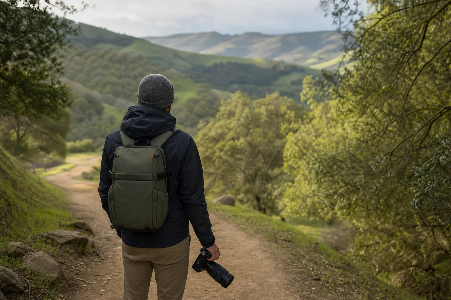 Fotograf mit Kamerarucksack beim Wandern auf einem malerischen Pfad durch eine grüne Landschaft