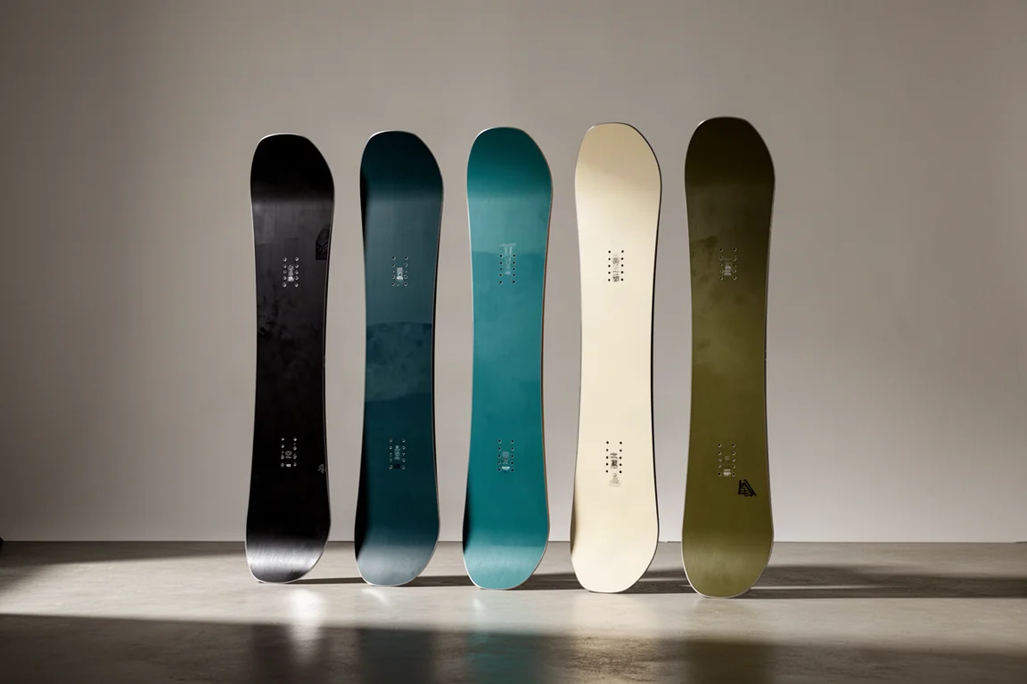 Five snowboards stood upright in a row against a neutral backdrop