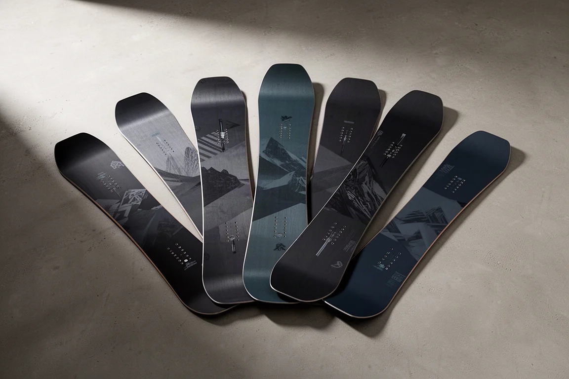 Huit snowboards disposés en éventail sur une surface en béton mat aux tons sourds