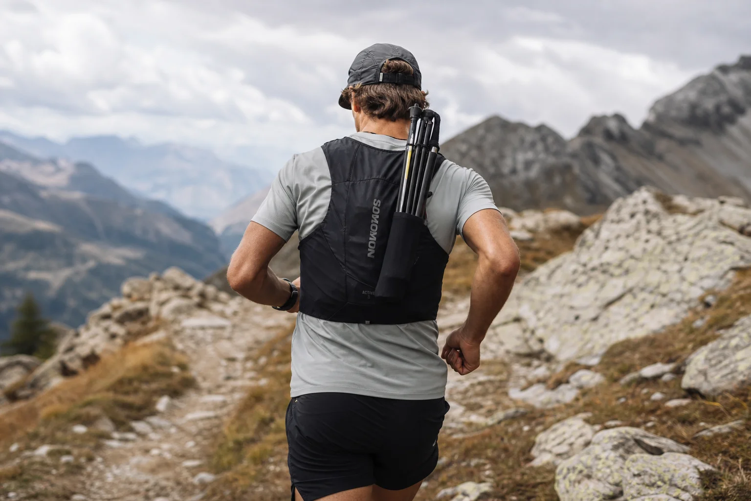 折りたたんだポールをクイバーに収納したランニングベストを着用するトレイルランナー