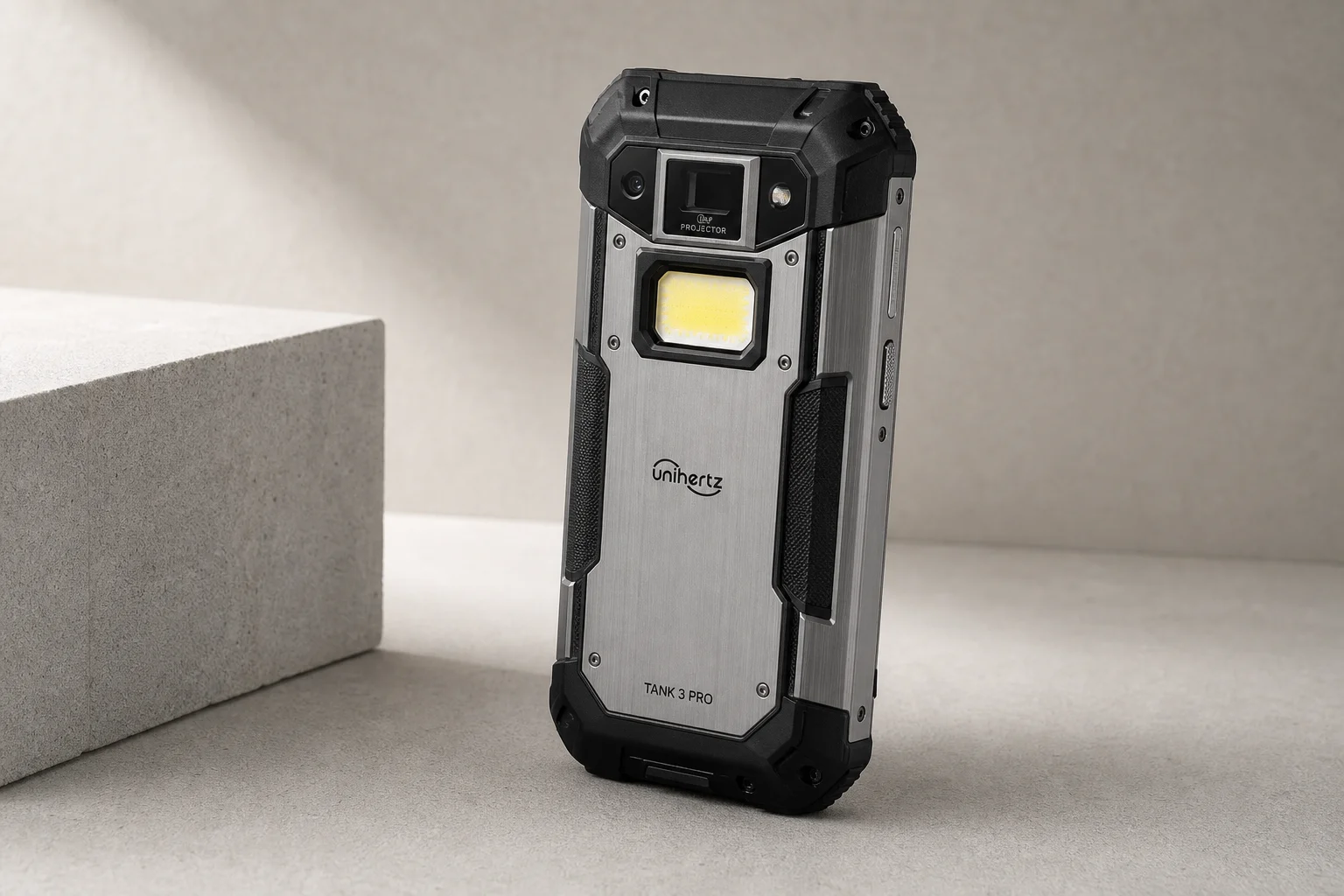 UniHertz Tank 3 Pro Outdoor-Smartphone auf Betonoberfläche mit sichtbarer Projektorlinse und LED-Taschenlampe