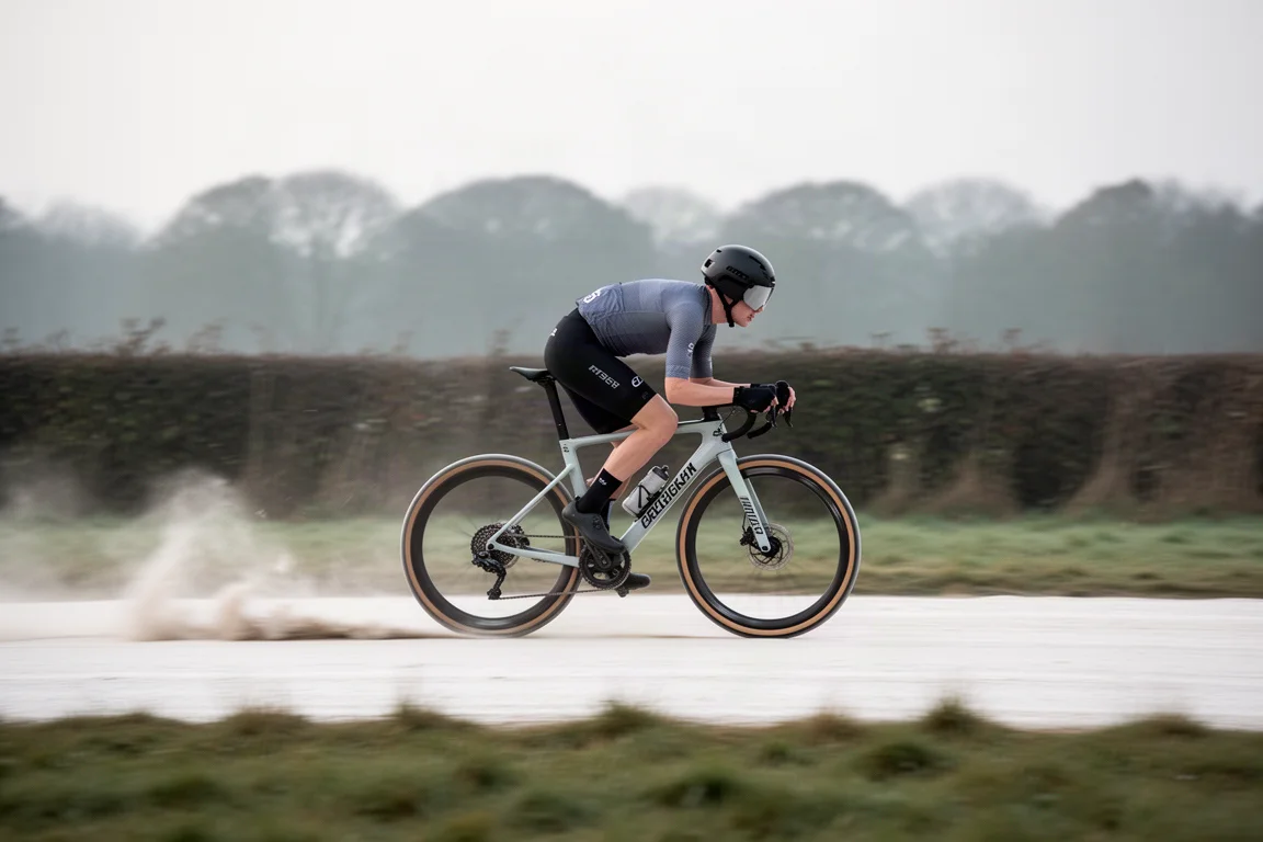 Wielrenner rijdt op hoge snelheid op een gravelracefiets over een krijtpad met opstuivend stof achter zich