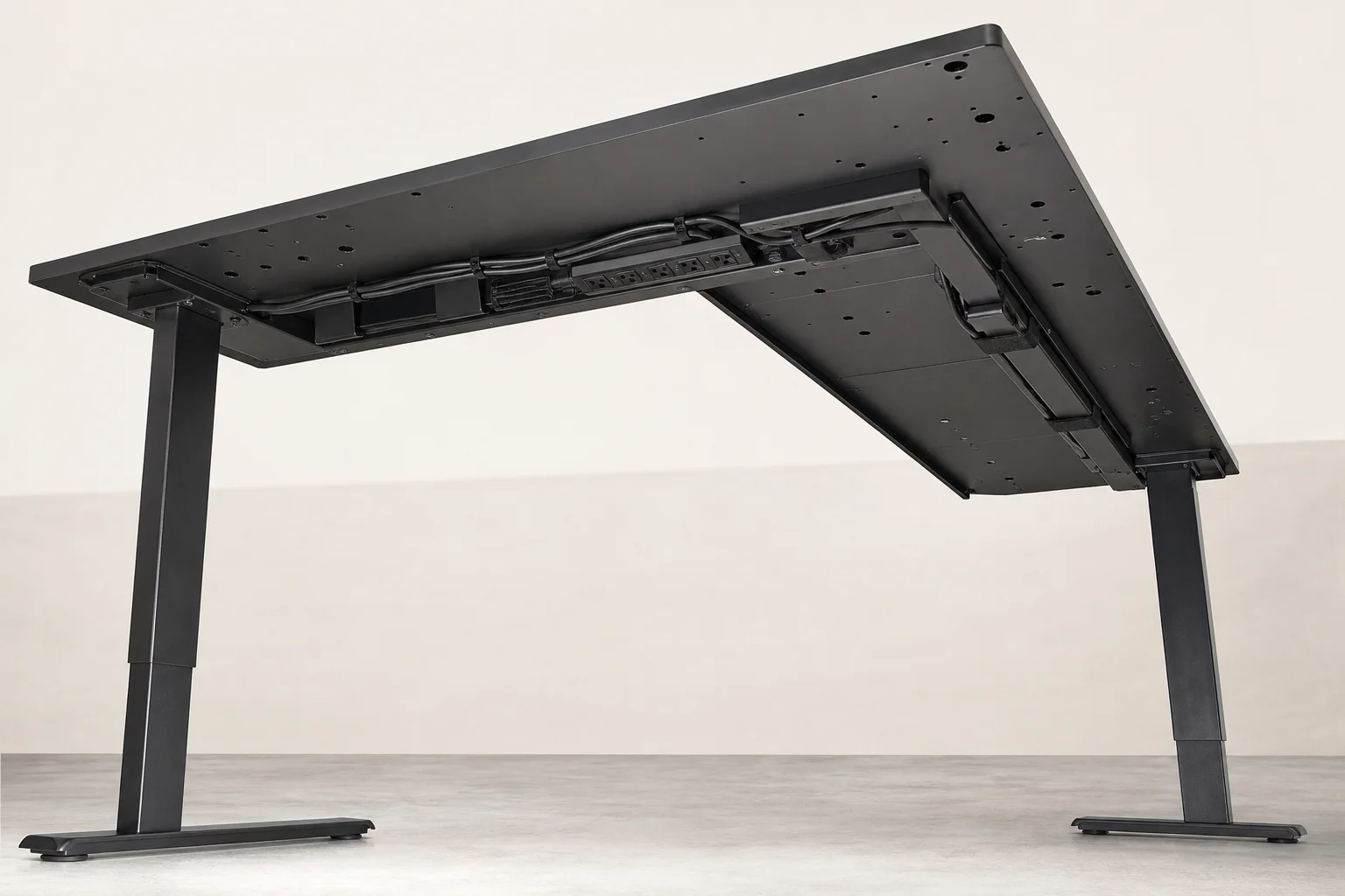 Underneath view of a standing desk showing cable management tray and pre-drilled mounting holes