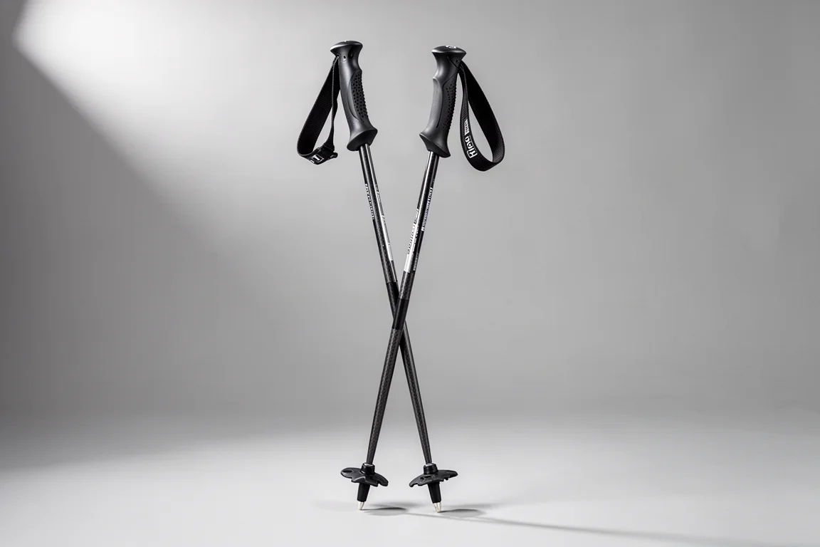 Pair of carbon ski poles with black grips and mid-width baskets on a grey backdrop