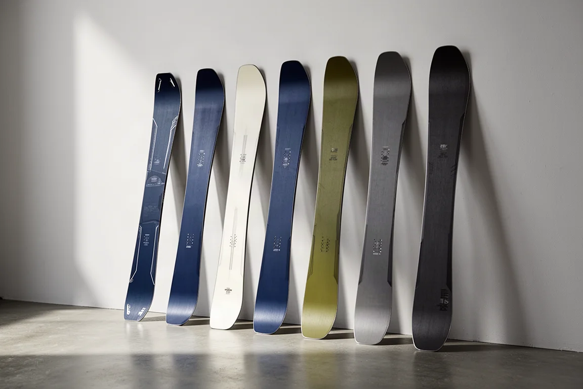 A row of wide powder skis of varying widths leaning against a pale studio wall