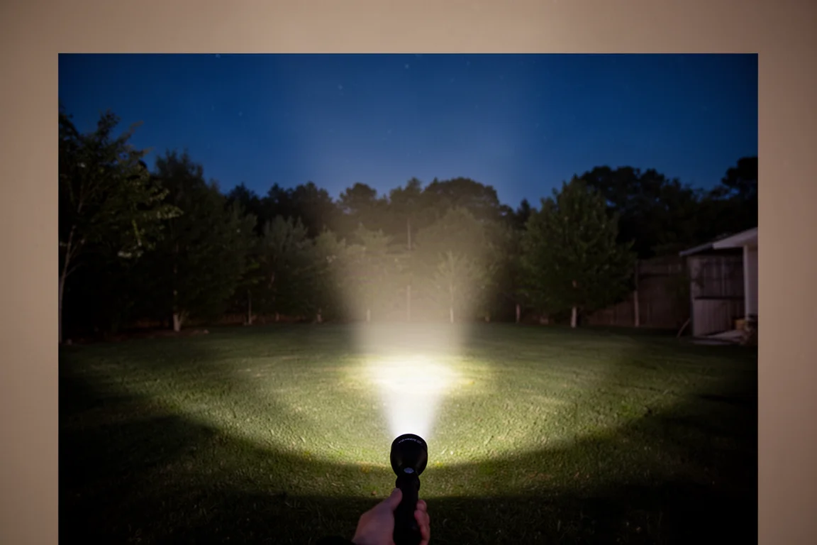 Flashlight beam on a backyard at night showing an even flood beam pattern